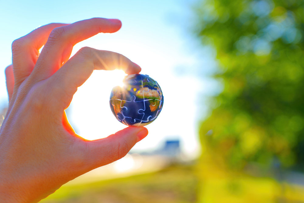 Hand hält kleine Weltkugel aus Puzzelteilen.